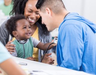 Mid adult Hispanic pediatrician talks with an adorable baby boy. The doctor is volunteering at a free community medical clinic.