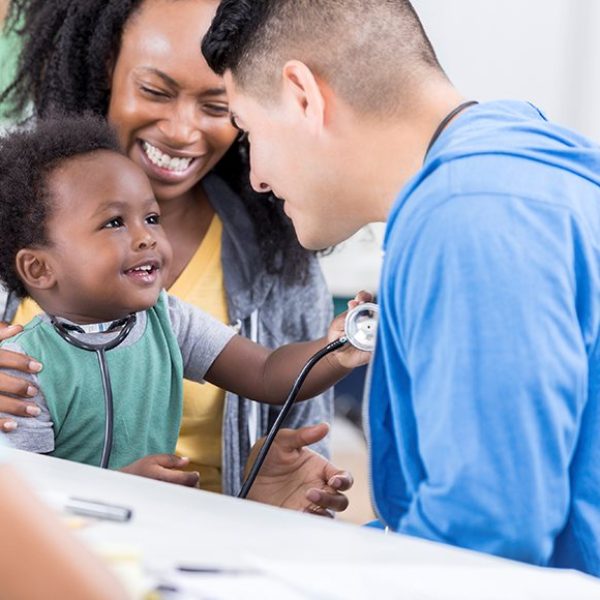 Mid adult Hispanic pediatrician talks with an adorable baby boy. The doctor is volunteering at a free community medical clinic.